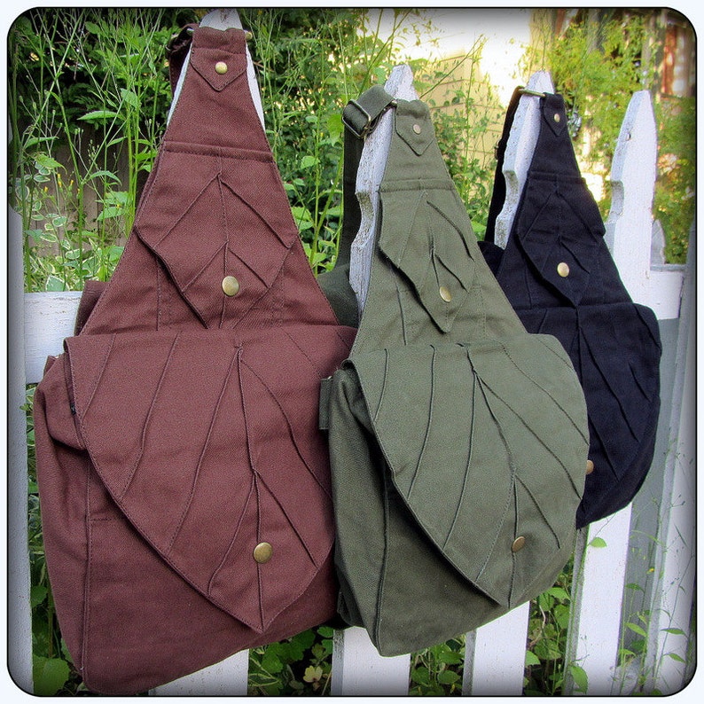 May include: Three canvas shoulder bags with leaf-shaped designs. The bags are brown, green, and black.