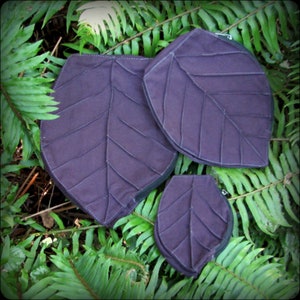 May include: Three purple leaf-shaped zippered pouches of different sizes. The pouches are made of fabric and have a quilted design.