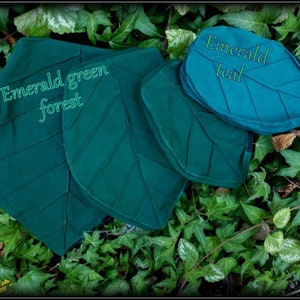 May include: Two leaf-shaped pouches made of fabric. The larger pouch is a dark green color and has the text "Emerald green forest" printed on it. The smaller pouch is a teal color and has the text "Emerald teal" printed on it.