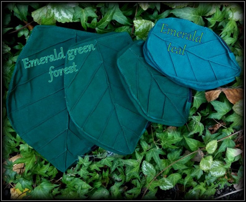 May include: Two leaf-shaped pouches made of fabric. The larger pouch is a dark green color and has the text "Emerald green forest" printed on it. The smaller pouch is a teal color and has the text "Emerald teal" printed on it.