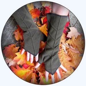 Könnte beinhalten: Ein Paar braune Fleece-Armwärmer mit einem Blatt-Muster. Die Armwärmer liegen auf einem Hintergrund aus Herbstblättern.