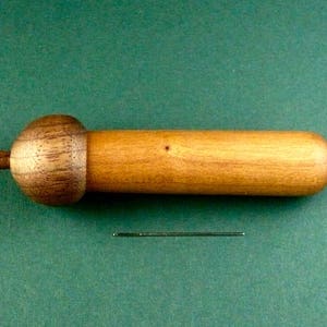 May include: A wooden acorn-shaped container with a smooth, light brown finish. The container is closed with a round, dark brown lid.