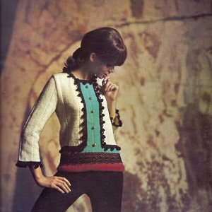 May include: A vintage-style jacket with a cream-colored textured weave, featuring a turquoise panel down the front with gold buttons. The jacket has black trim and a red and black waistband. The model is wearing black pants.