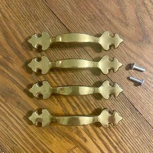 May include: Four gold-toned cabinet door pulls with ornate designs and two silver screws.