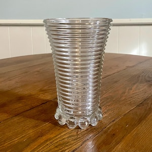 May include: A clear glass vase with a ribbed design and a scalloped base.
