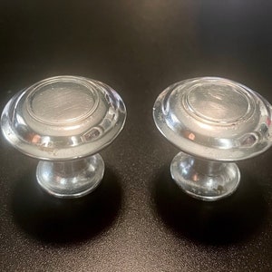 May include: Two silver cabinet knobs with a raised, circular design. The knobs have a smooth, shiny finish.