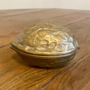 May include: A brass nutcracker in the shape of a walnut. The nutcracker is closed and has a detailed, textured surface.