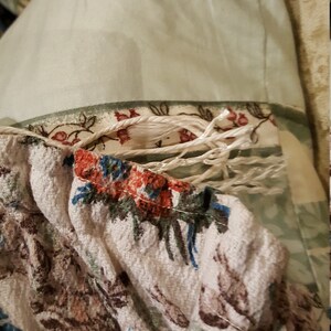 K&ouml;nnte beinhalten: Nahaufnahme eines wei&szlig;en Stoffes mit Blumenmuster. Der Stoff hat einen ausgefransten Rand und ist teilweise mit einem wei&szlig;en Seil bedeckt.