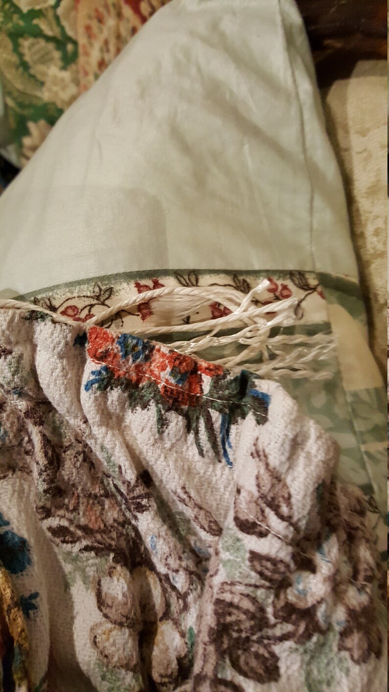 K&ouml;nnte beinhalten: Nahaufnahme eines wei&szlig;en Stoffes mit Blumenmuster. Der Stoff hat einen ausgefransten Rand und ist teilweise mit einem wei&szlig;en Seil bedeckt.