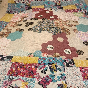 May include: A patchwork quilt featuring a range of floral patterns in shades of pink, blue, yellow, and red. The quilt is composed of squares and hexagons, and the fabric is a blend of cotton and linen.