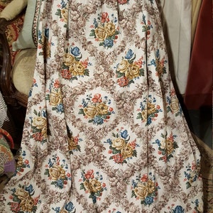 K&ouml;nnte beinhalten: Ein wei&szlig;er Stoffvorhang mit einem braunen Blumenmuster. Das Muster zeigt eine Vielzahl von Blumen, darunter Rosen, G&auml;nsebl&uuml;mchen und Tulpen. Die Blumen sind in den Farben Gelb, Rot, Blau und Gr&uuml;n gehalten.