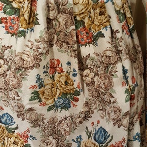 K&ouml;nnte beinhalten: Eine Nahaufnahme eines wei&szlig;en Stoffes mit einem Blumenmuster. Der Stoff zeigt eine Vielzahl von Blumen, darunter Rosen, Tulpen und kleinere Bl&uuml;ten. Die Blumen sind in den Farben Gelb, Rot, Blau und Braun gehalten.