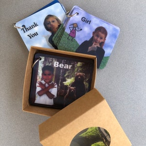 May include: A set of flashcards with images and words, including "Thank You", "Girl", and "Bear". The cards are bound with metal rings and presented in a brown cardboard box with an oval window.