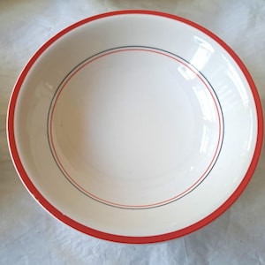 Puede incluir: Cuenco de cerámica blanco con borde rojo y una fina raya negra y roja. El cuenco tiene un diseño sencillo y clásico. La imagen muestra un primer plano del cuenco, destacando sus líneas limpias y colores brillantes. Este cuenco es adecuado para servir sopas, ensaladas u otros platos.