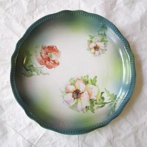May include: A vintage ceramic plate with a scalloped edge and a green glaze. The plate features a hand-painted floral design with pink, white, and red flowers.