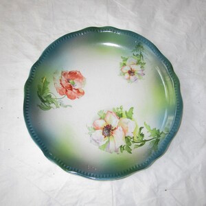 May include: A vintage porcelain plate with a scalloped edge and a green and white glaze. The plate features a hand-painted floral design with pink, white, and green flowers.