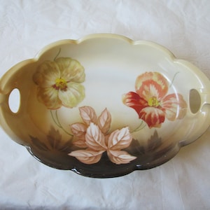 May include: An oval ceramic serving dish with two handles. The dish is decorated with a floral pattern featuring yellow, orange, and pink flowers with brown leaves on a cream background.