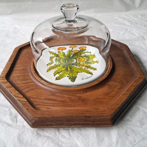 May include: A vintage wooden serving tray with a glass dome and a ceramic plate. The plate features a dandelion design with yellow and green colors. The tray is hexagonal and has a rich brown color.