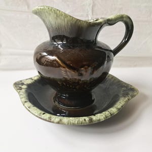 Peut inclure: Un ensemble composé d'un pot à lait en céramique et d'une soucoupe assortie, présentant un vernis brun foncé brillant avec un motif de gouttes vert clair le long du bord. Le pot possède une anse incurvée et un bec verseur.