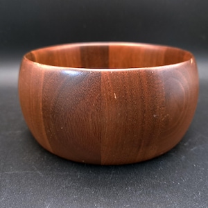 Puede incluir: Un cuenco redondo de madera de color marrón oscuro. El cuenco tiene una superficie lisa y pulida y un diseño sencillo y clásico. Este cuenco de madera es adecuado para servir ensaladas, frutas u otros platos.