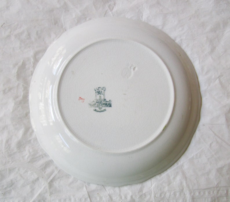May include: White ceramic plate with a scalloped edge. The back of the plate has a green and black castle logo with the text "Royal Doulton" printed below.