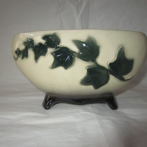 Puede incluir: Cuenco de cerámica color crema con diseño de hojas de hiedra verde oscuro. El cuenco tiene forma redondeada y se apoya en tres patas marrones oscuras. Un elemento decorativo para el hogar.