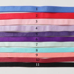 May include: Eleven elastic ribbons in a variety of colours are displayed. The colours are blue, red, pink, lavender, purple, dark purple, light green, light blue, peach, burgundy, and black. Each ribbon is a different colour and is numbered 1 to 11.