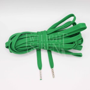 May include: Green shoelaces with silver aglets. The shoelaces are made of a woven fabric and are approximately 100 cm long.