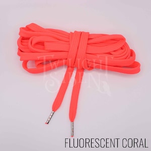 Puede incluir: Un par de cordones de zapatos de color coral fluorescente con aglets plateados. Los cordones est&aacute;n enrollados juntos.