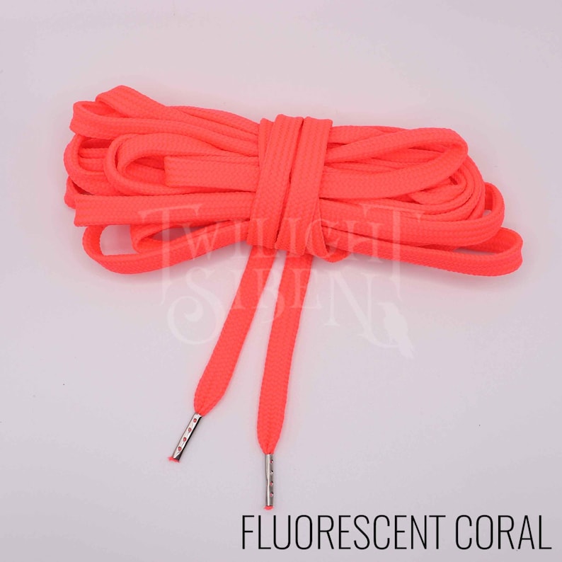 Puede incluir: Un par de cordones de zapatos de color coral fluorescente con aglets plateados. Los cordones est&aacute;n enrollados juntos.