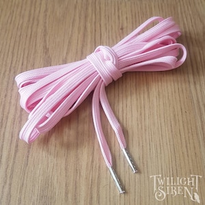 May include: Pink shoelaces with silver aglets. The shoelaces are coiled and tied together.