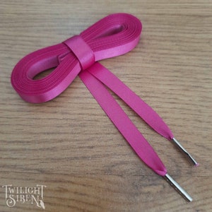 May include: Pink satin shoelaces with silver metal aglets. The shoelaces are tied in a bow.