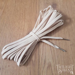 May include: A pair of beige shoelaces with silver aglets. The shoelaces are coiled and tied together.