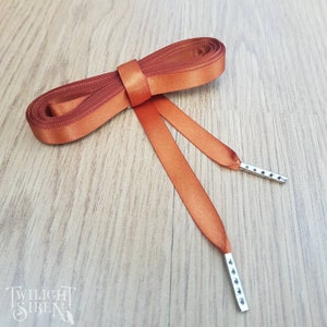May include: A pair of orange satin ribbon shoelaces with silver metal aglets. The laces are tied together in a bow.