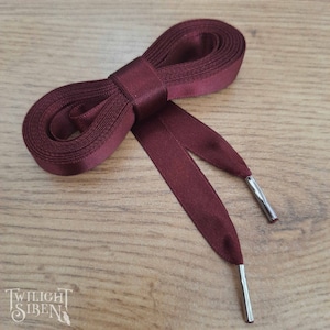 May include: Burgundy satin shoelaces with silver metal aglets. The shoelaces are tied in a bow.