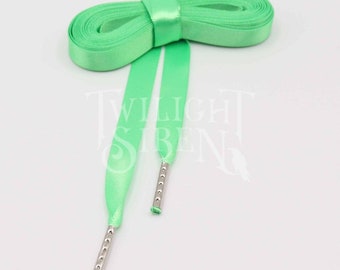 May include: A pair of green satin shoelaces with silver aglets. The laces are tied together in a bow.