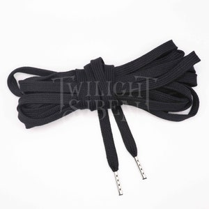 May include: Black shoelaces with silver aglets, neatly arranged against a white background. The flat, woven laces are knotted in the middle, with the aglets visible at the ends. The shoelaces are a solid black color.