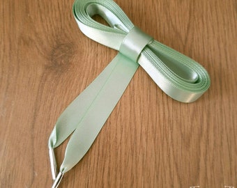 May include: A light green satin ribbon with silver metal tips. The ribbon is tied in a bow.