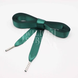 Peut inclure: Une paire de lacets de chaussures en satin vert émeraude avec des embouts en métal argenté. Les lacets sont noués en un nœud.