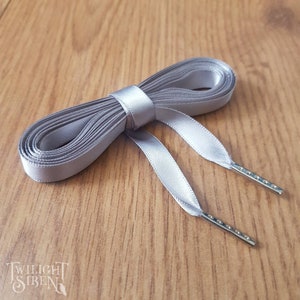 May include: A pair of silver satin shoelaces with metal aglets. The laces are tied together in a bow.