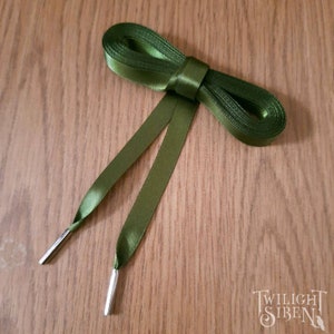 May include: A pair of green satin shoelaces with silver metal aglets. The laces are tied in a bow.