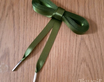 May include: A pair of green satin shoelaces with silver metal aglets. The laces are tied in a bow.
