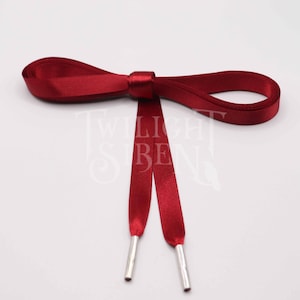 May include: A pair of red satin shoelaces with silver aglets. The laces are tied in a bow.