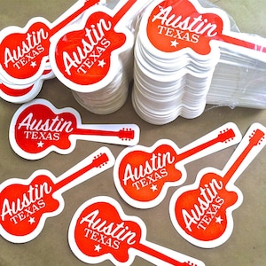 May include: A stack of red and white guitar-shaped stickers with the text "Austin Texas" on each sticker.