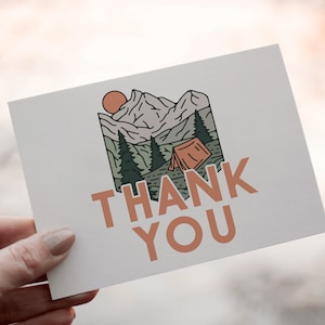 May include: A thank you card with a hand-drawn illustration of a mountain range with a tent and a sun. The text "THANK YOU" is written in a brown font.