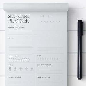 May include: A white self-care planner with sections for daily affirmations, to-do lists, water intake, sleep, mood, gratitude, notes, and reminders. The planner also includes a section for tomorrow's plans.