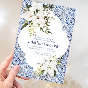 Puede incluir: Una invitación de ducha nupcial blanca con un borde de azulejos azules y blancos. La invitación presenta un diseño floral con flores blancas y hojas verdes. El texto dice "Por favor, únase a nosotros para una despedida de soltera en honor a Adeline Richard, domingo, 6 de abril a las 2:00 PM, 555 Julie Lane, Lafayette, LA 70508, RSVP al 555-555-5555, Registrado en Target."