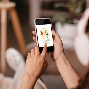 May include: A smartphone displaying a digital invitation for a holiday party. The invitation features a festive illustration of three cocktails with colorful garnishes and the text "Making Spirits Bright".