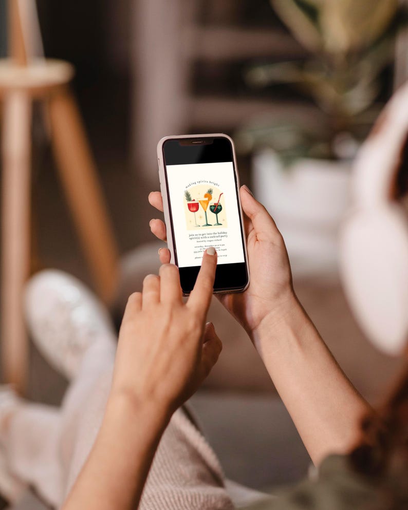 May include: A smartphone displaying a digital invitation for a holiday party. The invitation features a festive illustration of three cocktails with colorful garnishes and the text "Making Spirits Bright".
