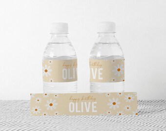 May include: Two clear plastic water bottles with labels that say "Happy Birthday Olive" and feature a white daisy pattern on a beige background. A matching label with the same design is also shown.